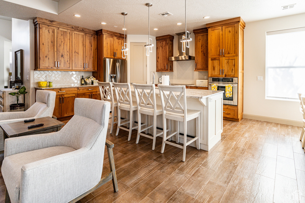 Kitchen with visible vents, appliances with stainless steel finishes, brown cabinetry, and wall chimney exhaust hood