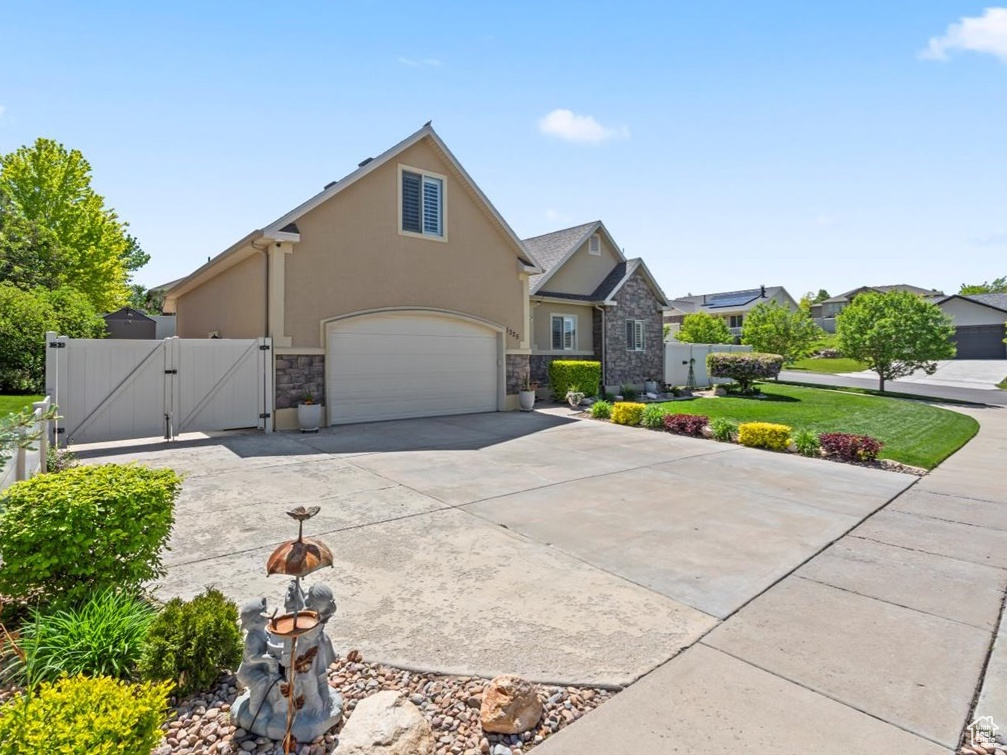 View of front facade featuring a gate, stone siding, stucco siding, concrete driveway, and an attached garage