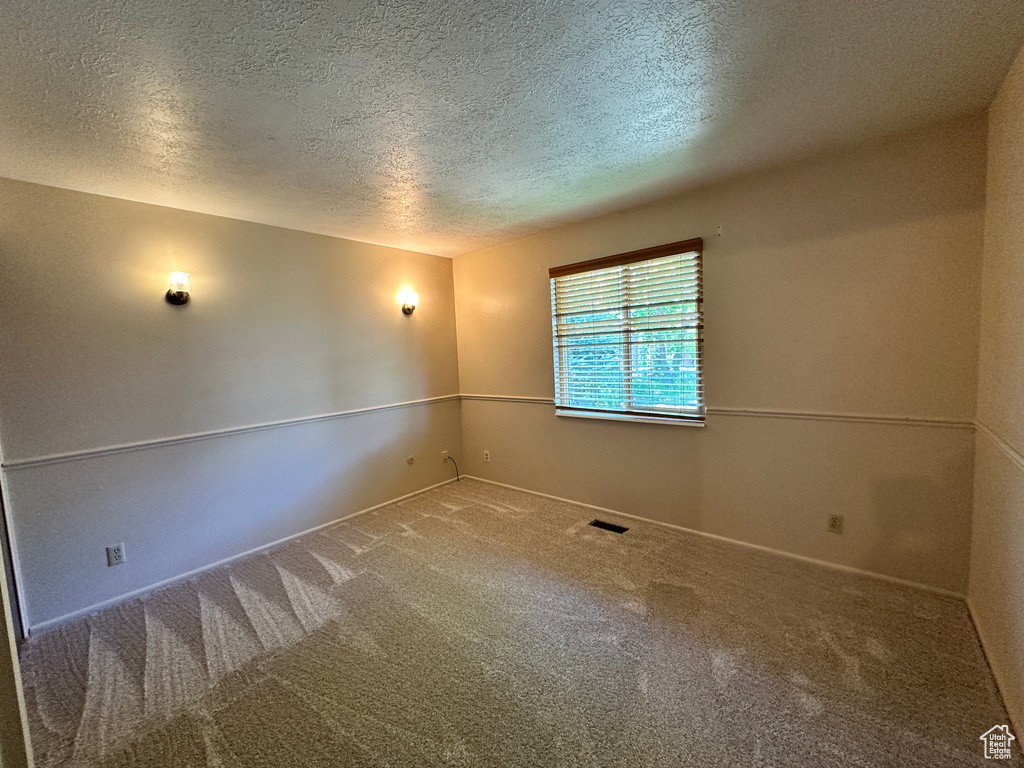 Empty room featuring a textured ceiling, carpet flooring, and baseboards