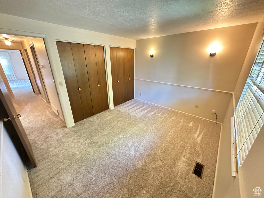 Unfurnished bedroom featuring a textured ceiling, multiple closets, and carpet flooring