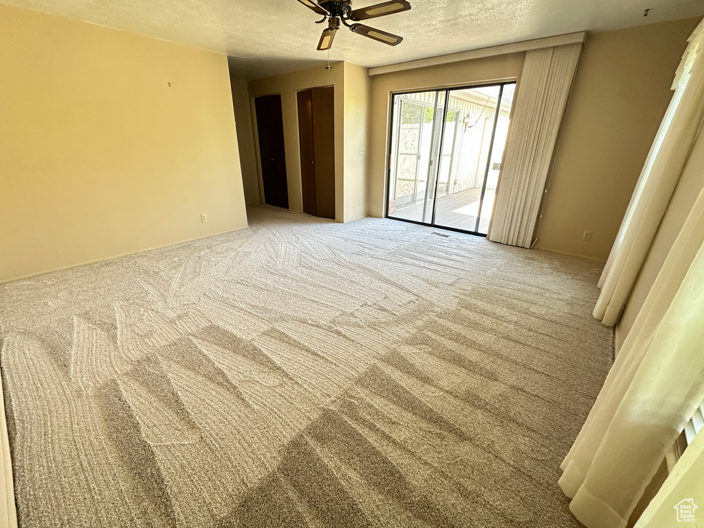 Carpeted empty room with a ceiling fan and a textured ceiling