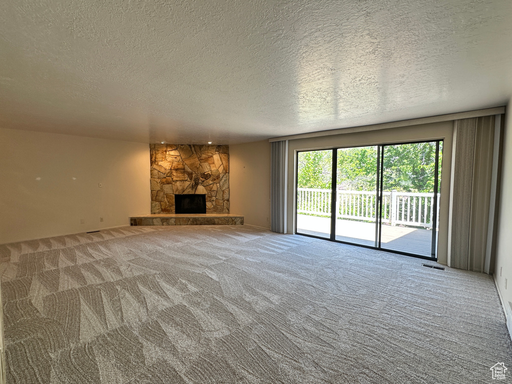Unfurnished living room with carpet flooring, a textured ceiling, and a fireplace