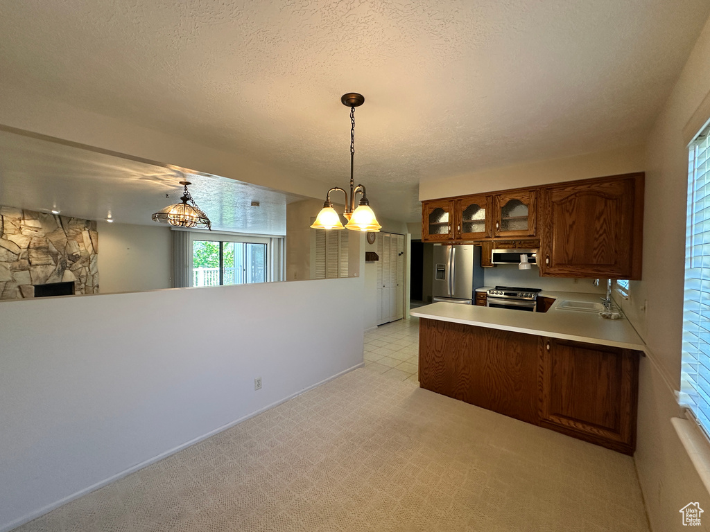 Kitchen with appliances with stainless steel finishes, a peninsula, a sink, glass insert cabinets, and light countertops