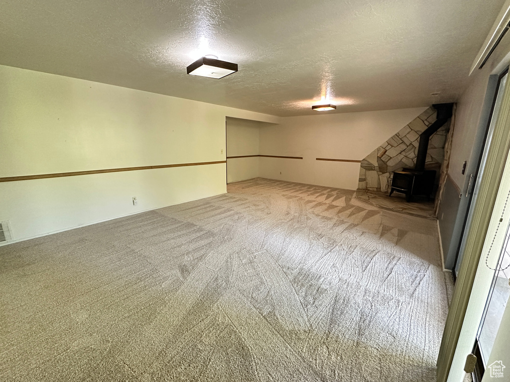Finished basement featuring a textured ceiling, a wood stove, and carpet