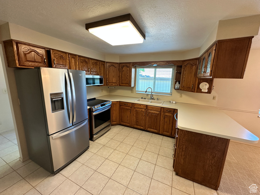 Kitchen featuring appliances with stainless steel finishes, a peninsula, a sink, a textured ceiling, and light countertops