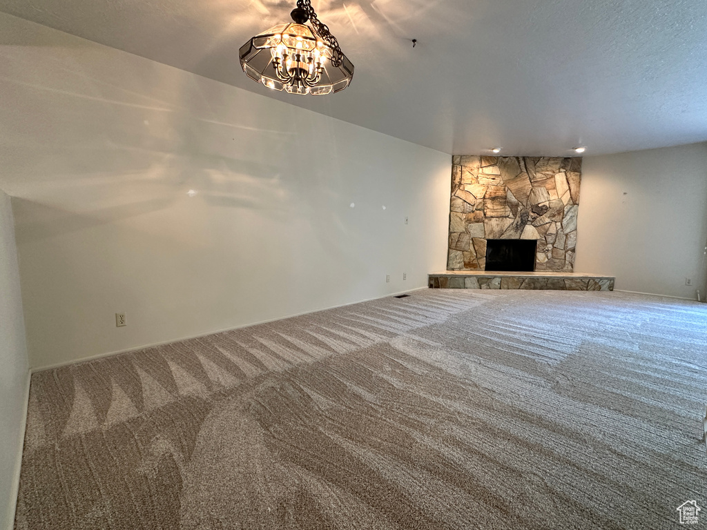 Unfurnished living room with carpet flooring, a stone fireplace, a chandelier, and baseboards