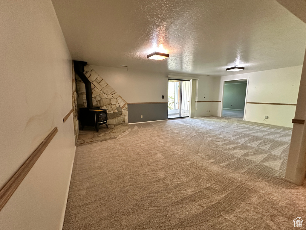 Unfurnished living room with a textured ceiling, carpet floors, and a wood stove