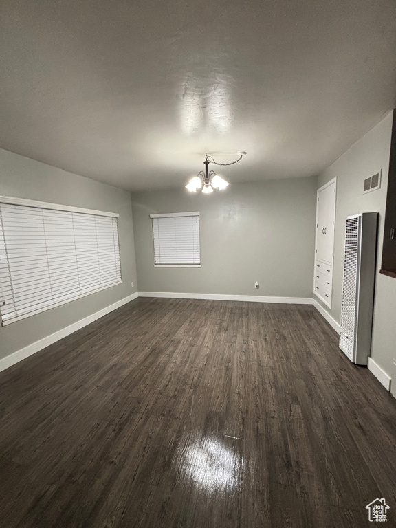 Empty room featuring baseboards, dark wood-style flooring, visible vents, and an inviting chandelier