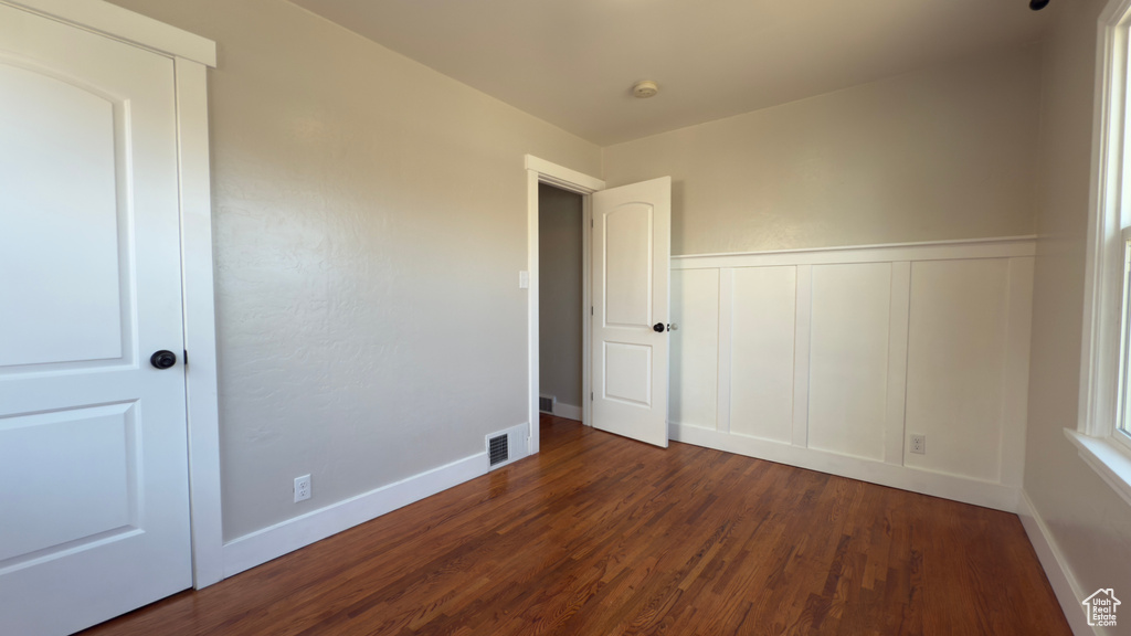 Unfurnished bedroom featuring a decorative wall, visible vents, baseboards, wood finished floors, and wainscoting