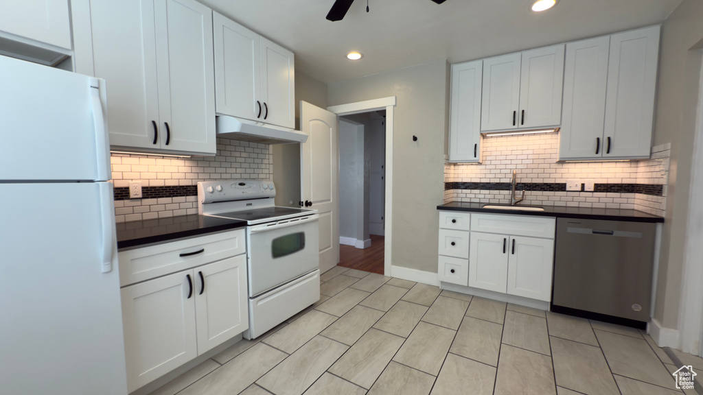 Kitchen with white appliances, ceiling fan, dark countertops, under cabinet range hood, and a sink