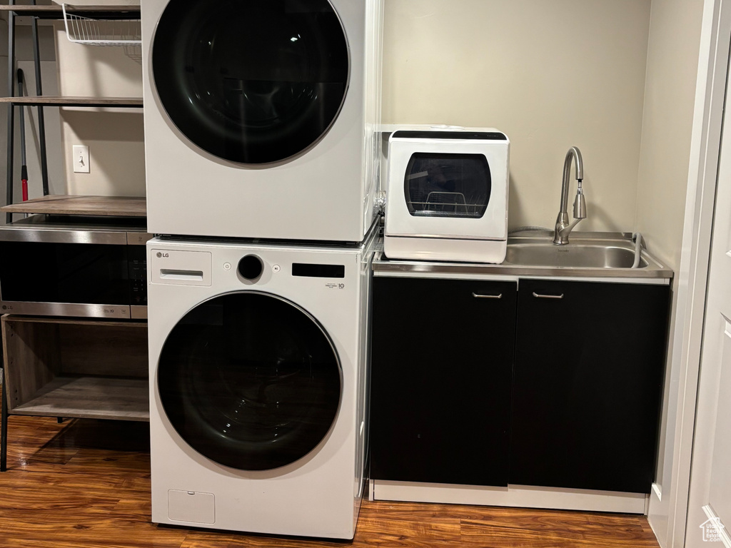 Clothes washing area with stacked washer / drying machine, laundry area, recessed lighting, wood finished floors, and a sink