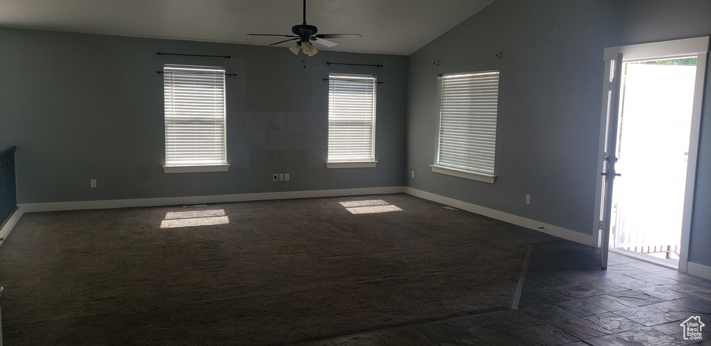 Spare room featuring lofted ceiling, baseboards, a ceiling fan, dark stone finish flooring, and dark colored carpet