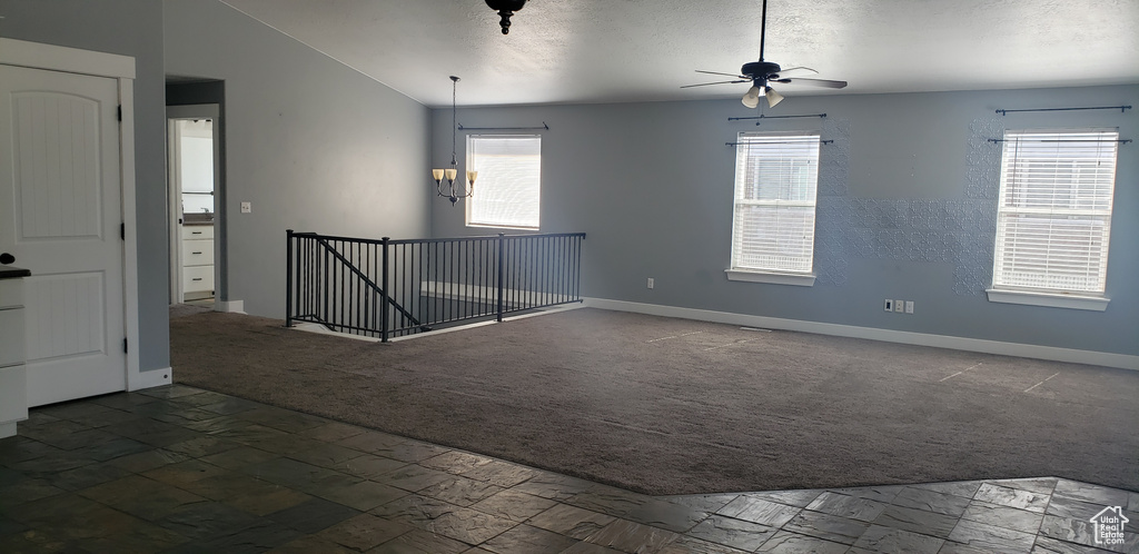 Carpeted empty room featuring healthy amount of natural light, baseboards, ceiling fan, and vaulted ceiling