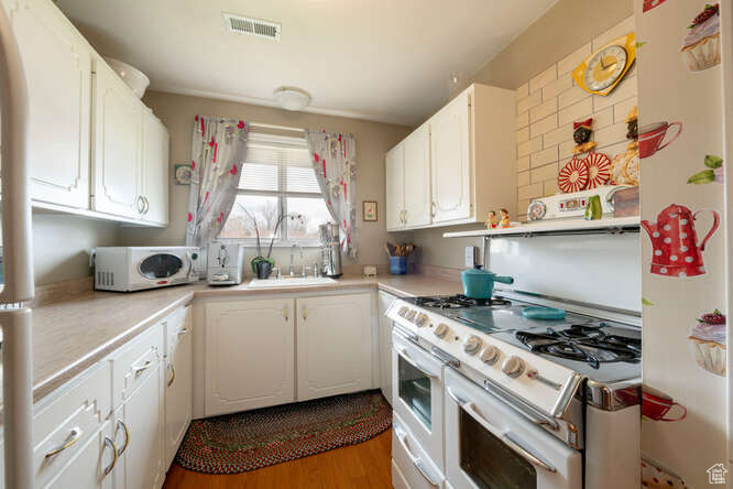 Kitchen with light countertops, a sink, white appliances, visible vents, and white cabinets
