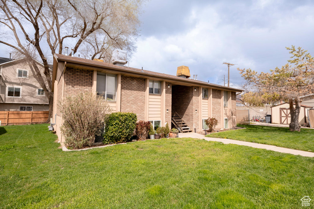 Exterior space featuring an outdoor structure, brick siding, fence, and a front lawn