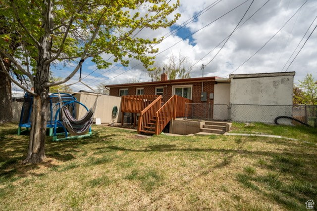Rear view of property with fence, brick siding, a wooden deck, a chimney, and a yard