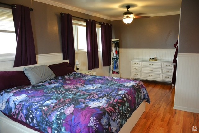 Bedroom with crown molding, wood finished floors, and wainscoting