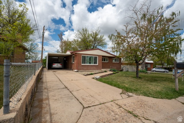 Bungalow-style house with fence, a front lawn, brick siding, an attached carport, and driveway