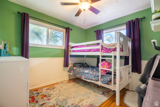 Bedroom featuring a wainscoted wall, ceiling fan, a textured ceiling, and wood finished floors