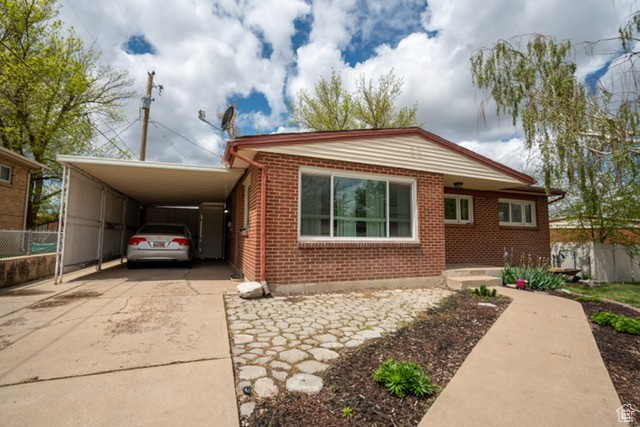 View of front of home with concrete driveway, brick siding, fence, and a carport