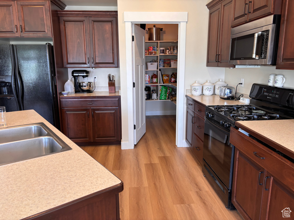 Kitchen featuring black appliances, light wood-type flooring, light countertops, and a sink