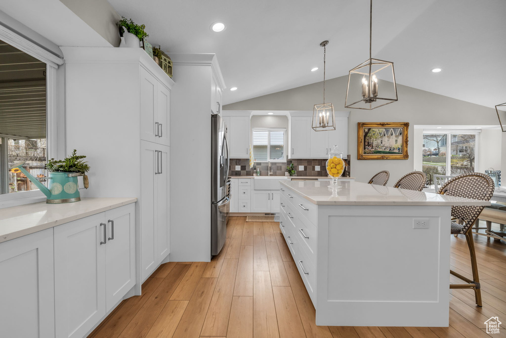 Kitchen featuring stainless steel refrigerator with ice dispenser, light wood finished floors, a center island, and a breakfast bar area