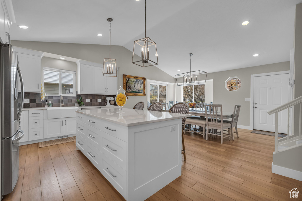 Kitchen with stainless steel fridge with ice dispenser, tasteful backsplash, light wood-style flooring, a center island, and lofted ceiling