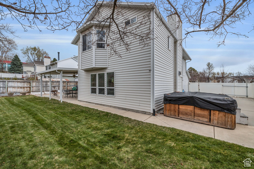 Back of property with a yard, a patio area, a fenced backyard, and a hot tub