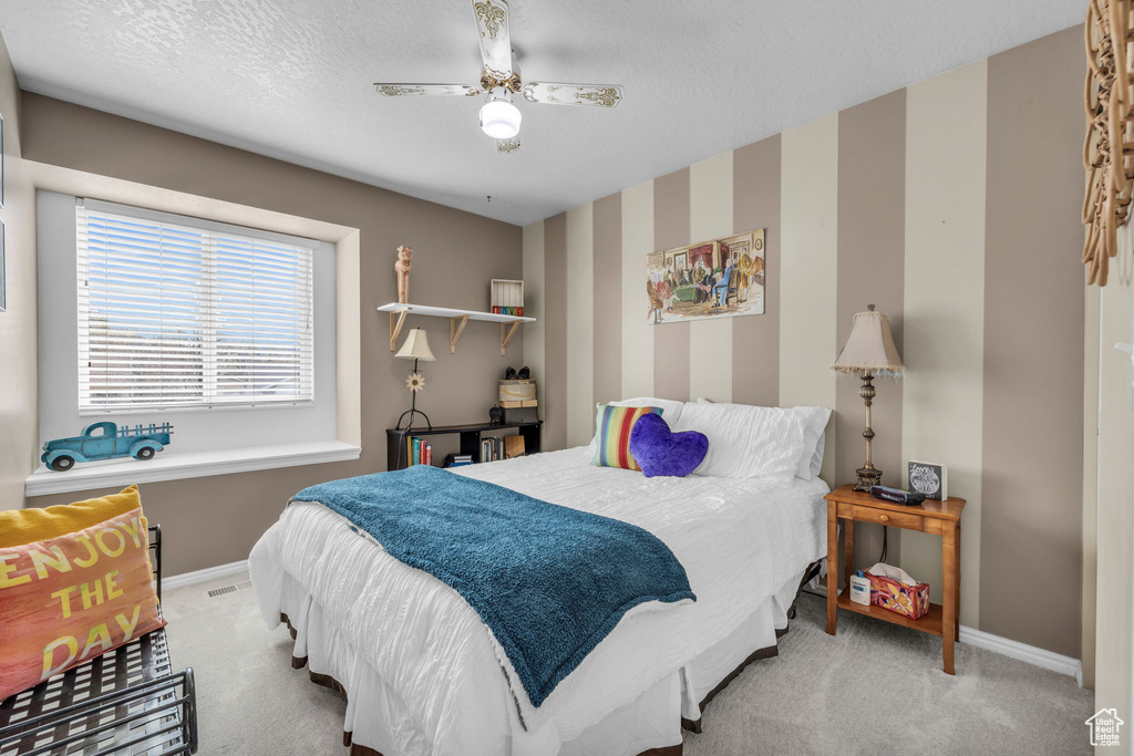 Carpeted bedroom with a textured ceiling, wallpapered walls, baseboards, and visible vents