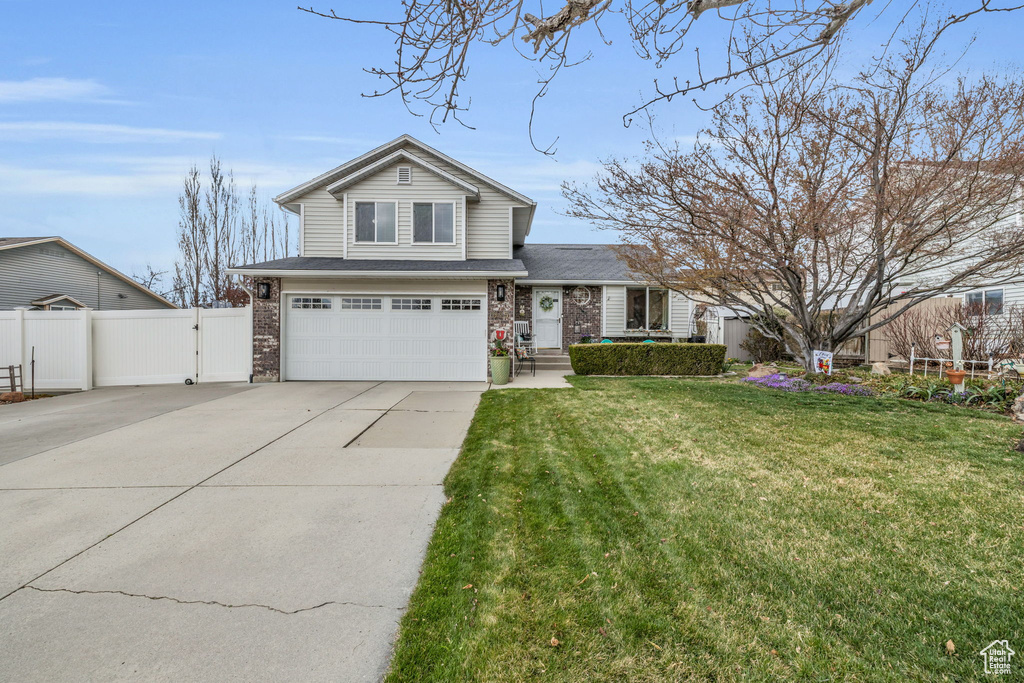 Traditional-style home featuring fence, a front lawn, a gate, an attached garage, and driveway