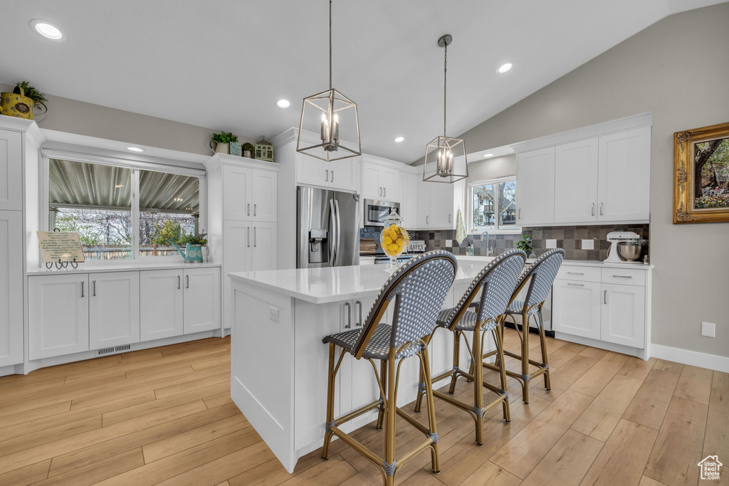 Kitchen featuring hanging light fixtures, light countertops, appliances with stainless steel finishes, light wood-style floors, and white cabinetry