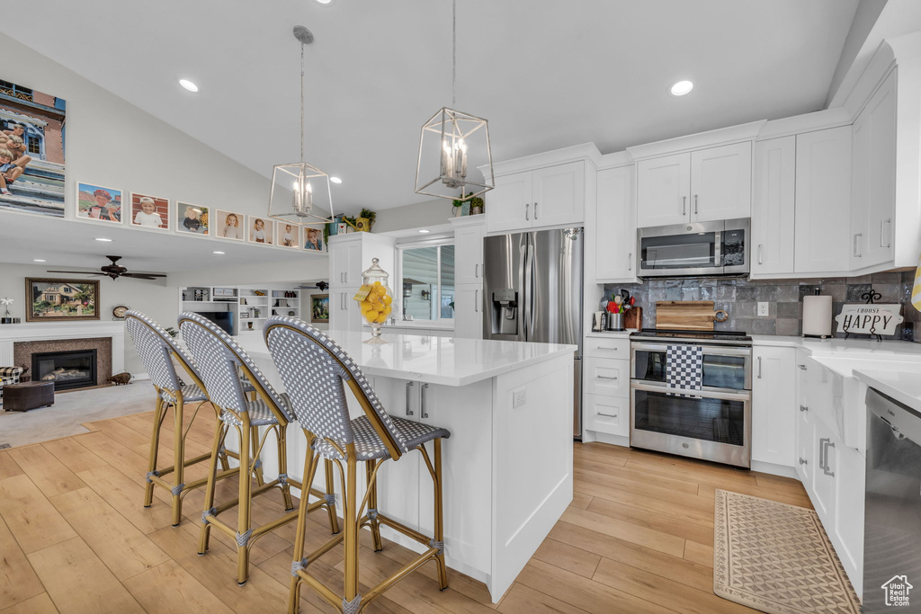 Kitchen featuring ceiling fan, white cabinets, appliances with stainless steel finishes, open floor plan, and light wood finished floors