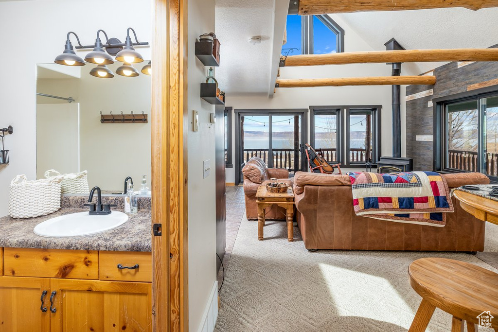 Living room with carpet flooring, plenty of natural light, vaulted ceiling with beams, and a wood stove