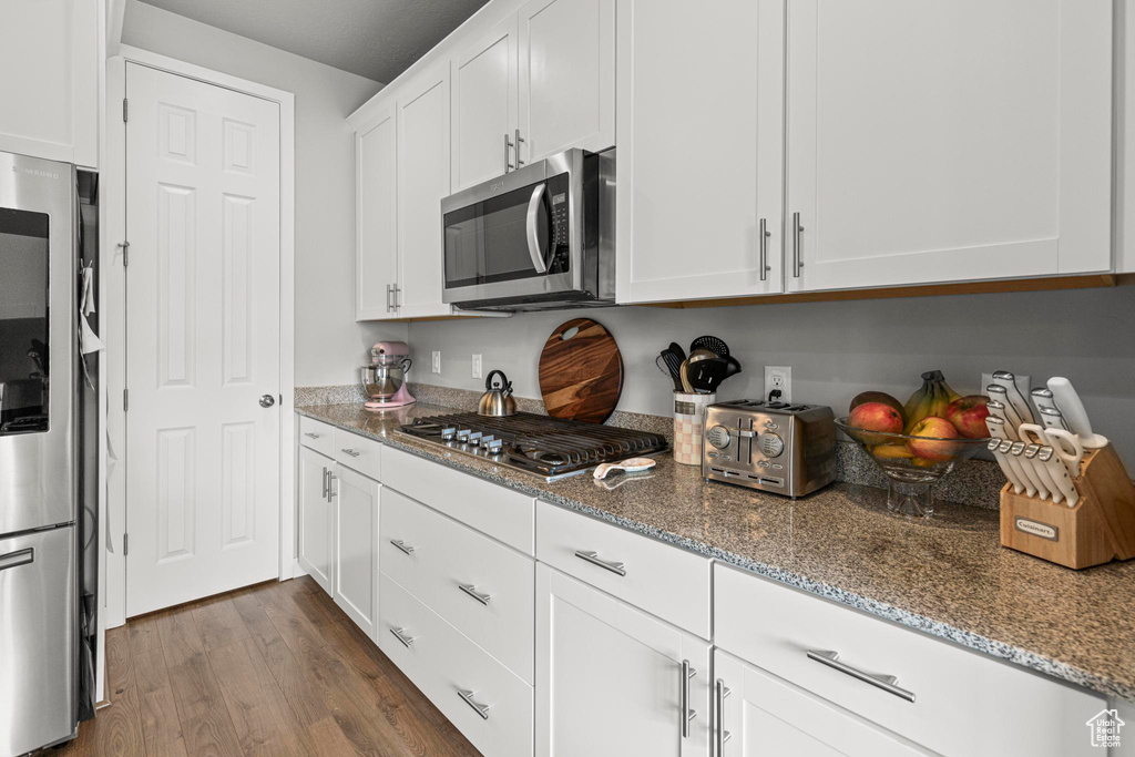 Kitchen featuring appliances with stainless steel finishes, white cabinets, light stone countertops, and dark wood-style floors