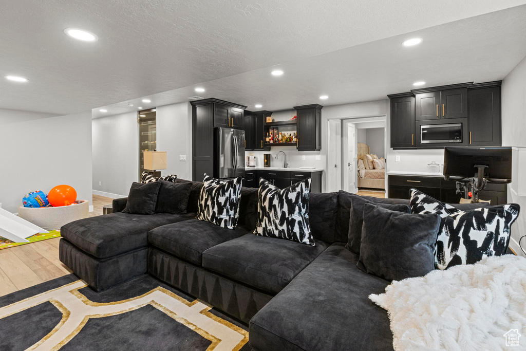 Living area featuring recessed lighting, bar with sink, light wood-style flooring, and baseboards