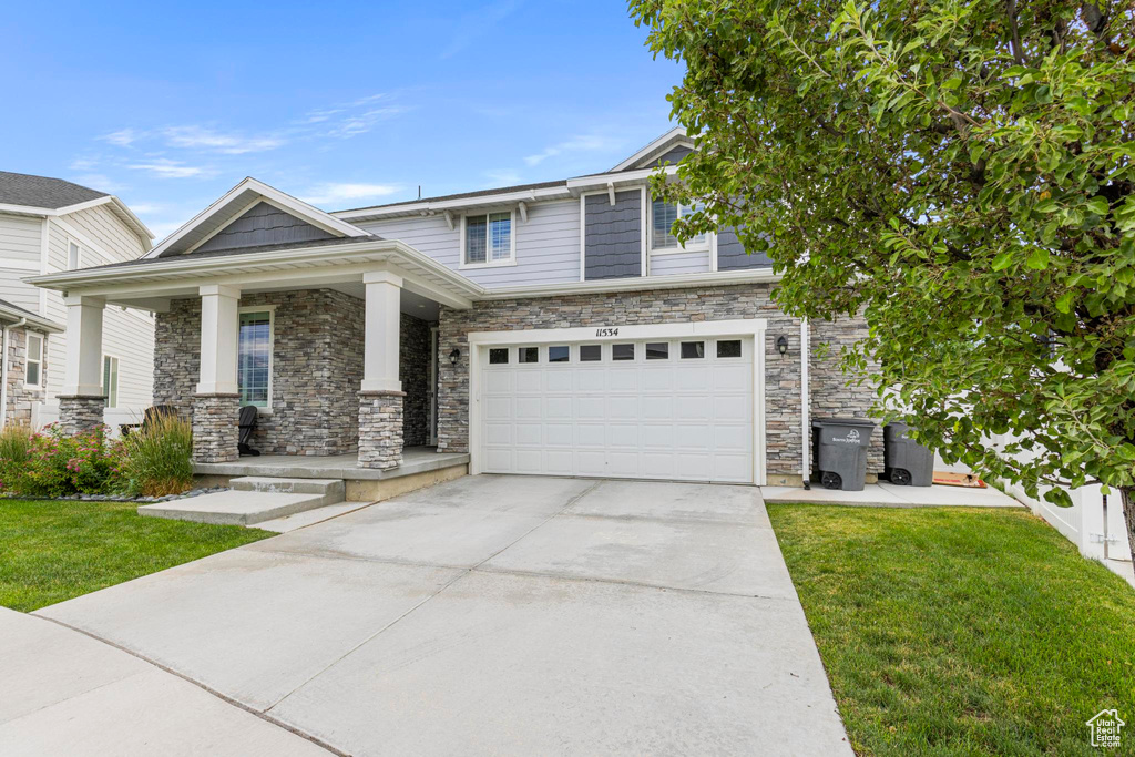 View of front facade featuring a porch, driveway, a front lawn, and an attached garage