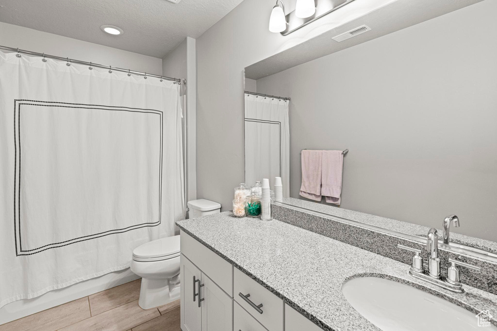 Full bathroom featuring toilet, vanity, a textured ceiling, and wood finished floors
