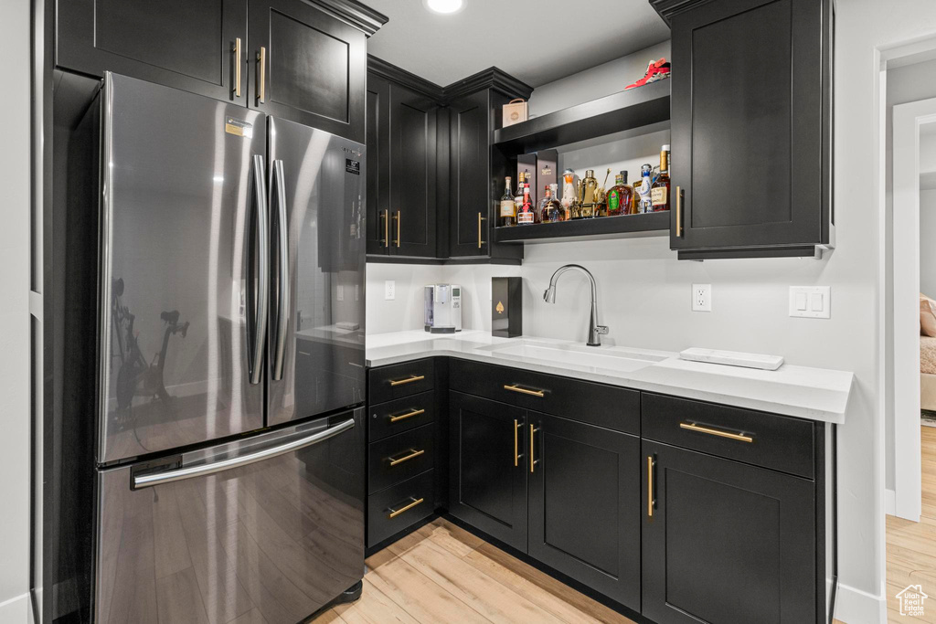 Kitchen featuring freestanding refrigerator, a sink, dark cabinetry, and light wood-style flooring