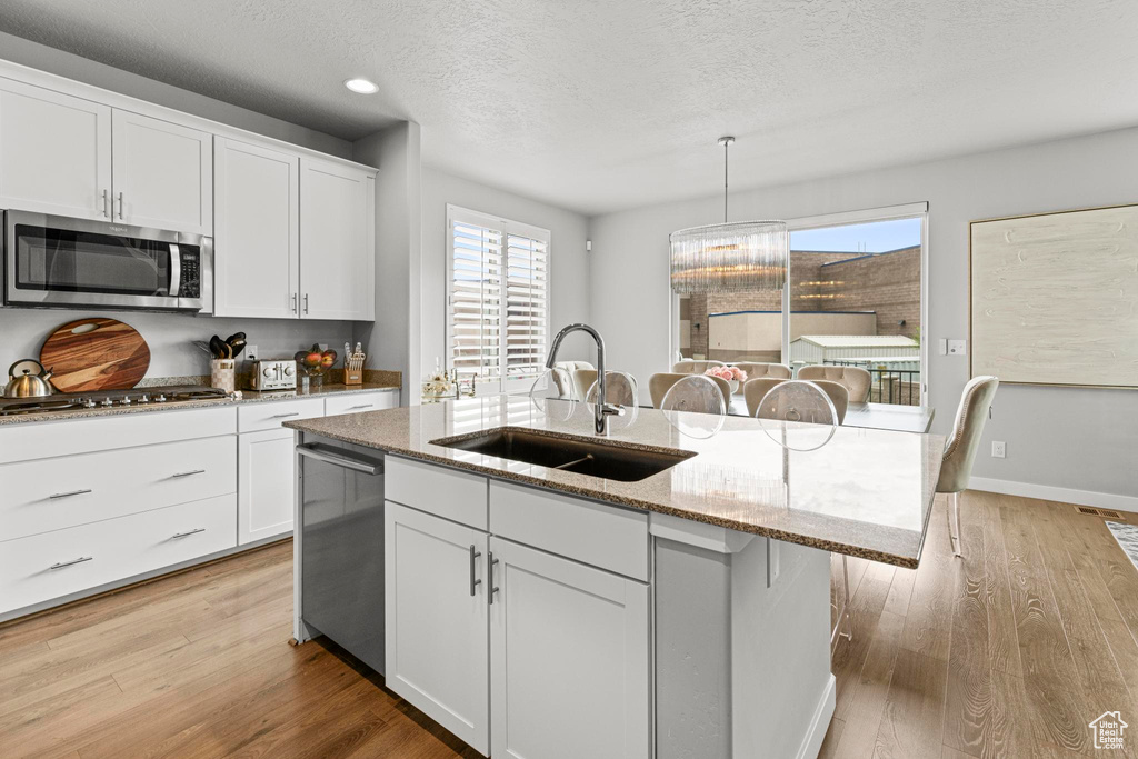 Kitchen featuring stainless steel appliances, a sink, light wood-style flooring, an island with sink, and a textured ceiling