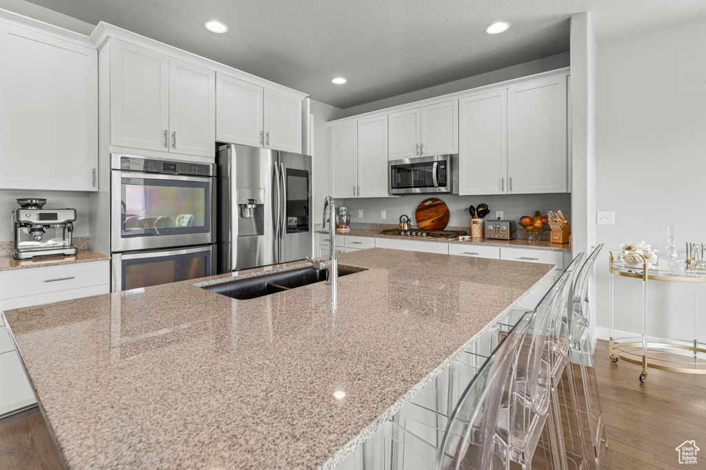 Kitchen with appliances with stainless steel finishes, wood finished floors, a center island with sink, recessed lighting, and white cabinets