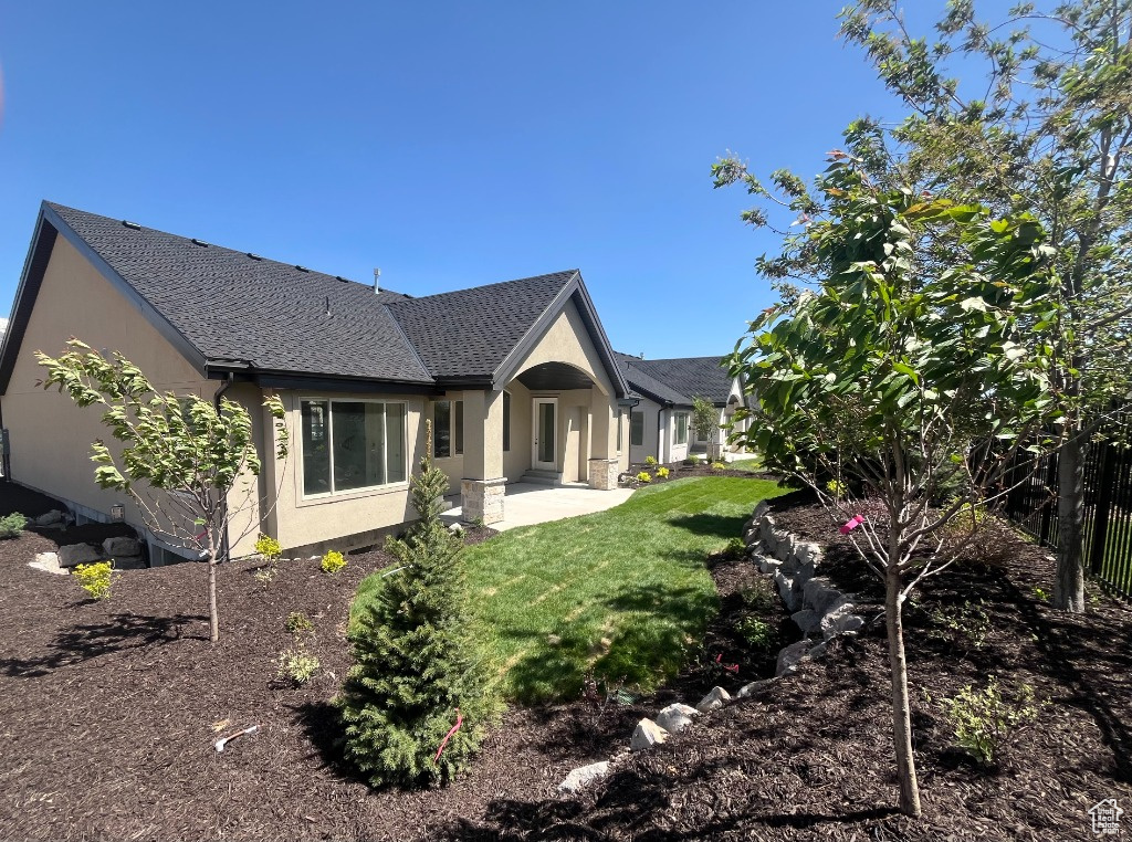 Back of house with stucco siding, a yard, a patio, and a shingled roof