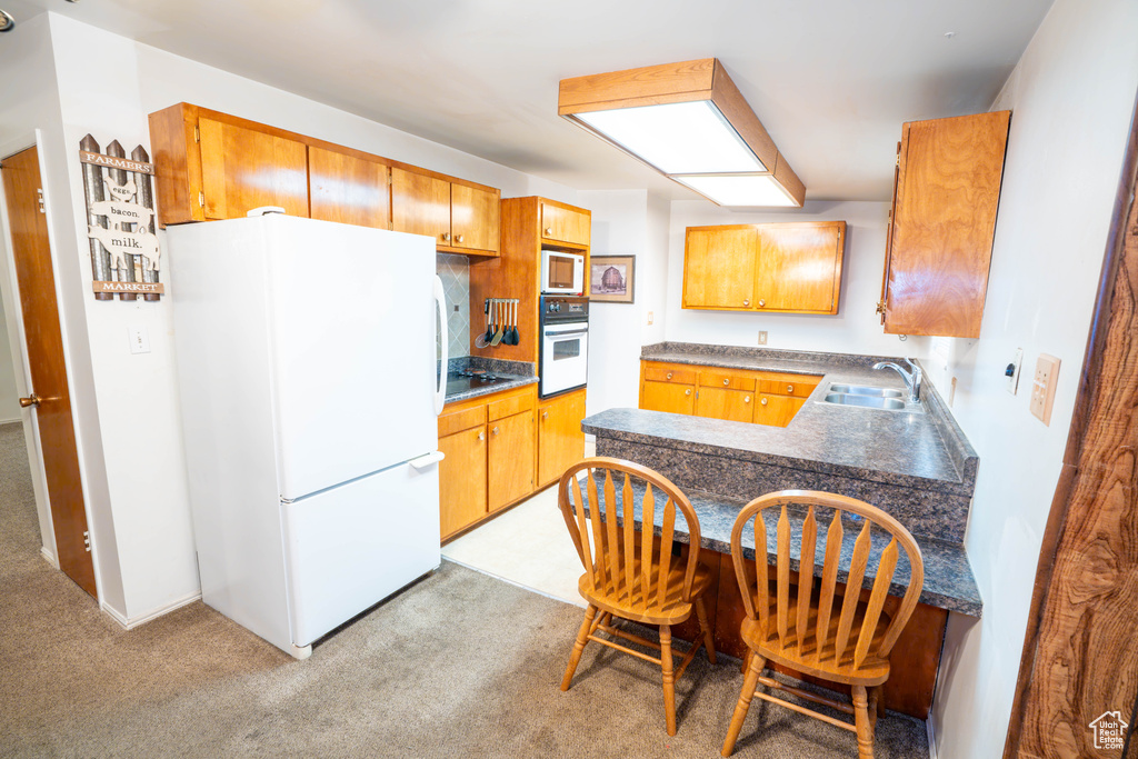 Kitchen with white appliances, a sink, light colored carpet, and a peninsula