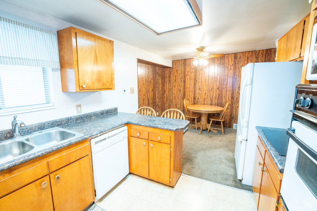 Kitchen featuring white appliances, a peninsula, ceiling fan, a sink, and wooden walls