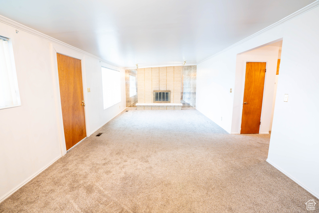 Unfurnished living room featuring carpet, ornamental molding, a fireplace, and baseboards