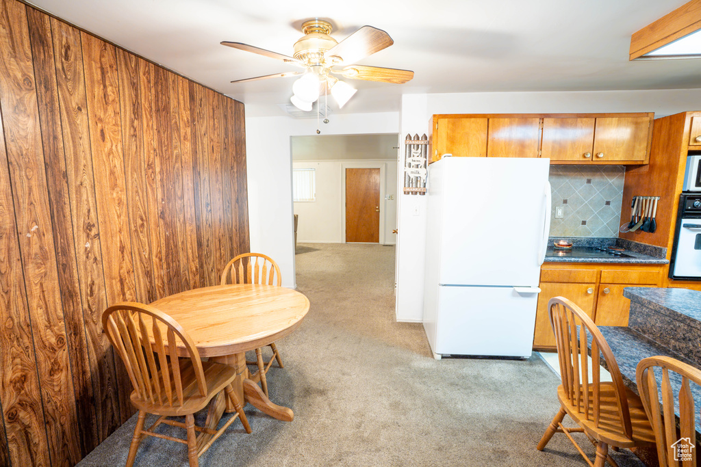 Kitchen with white appliances, light colored carpet, dark countertops, brown cabinets, and tasteful backsplash