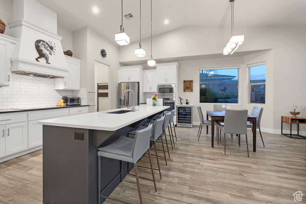Kitchen featuring tasteful backsplash, light wood-type flooring, a sink, beverage cooler, and stainless steel appliances