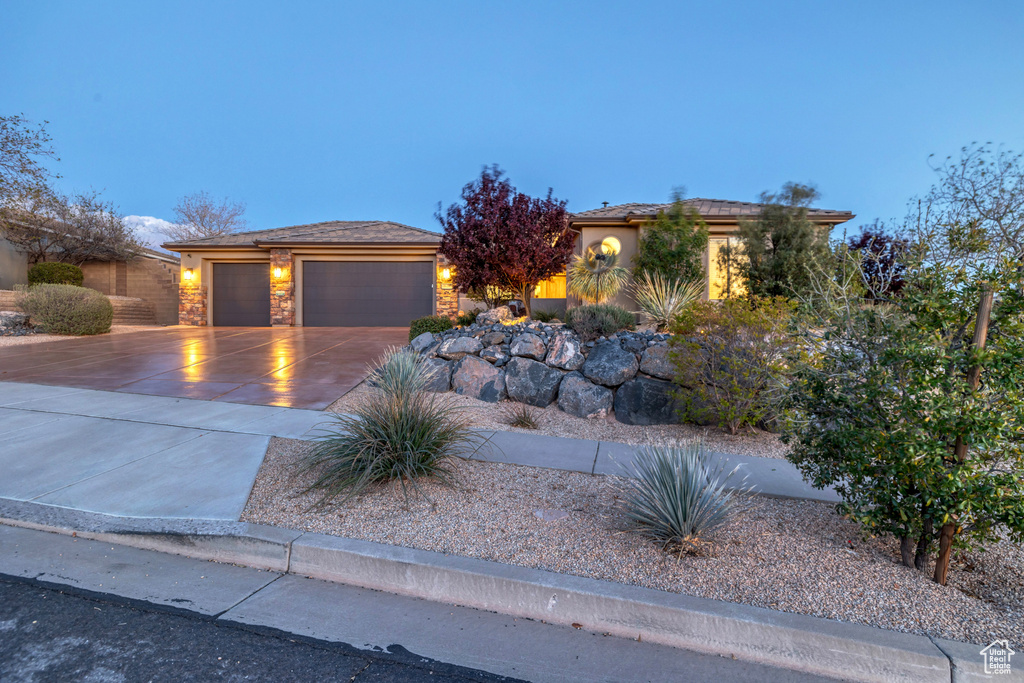 View of front of house with an attached garage, stone siding, driveway, and stucco siding