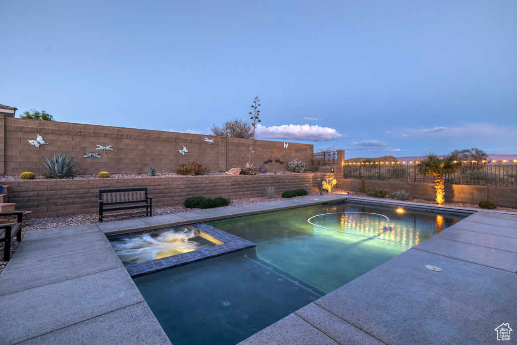 Pool at dusk featuring a patio, a fenced backyard, and a pool with connected hot tub