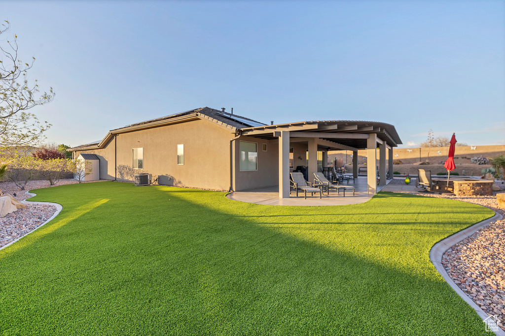 Rear view of house with a patio area, roof mounted solar panels, a yard, and stucco siding
