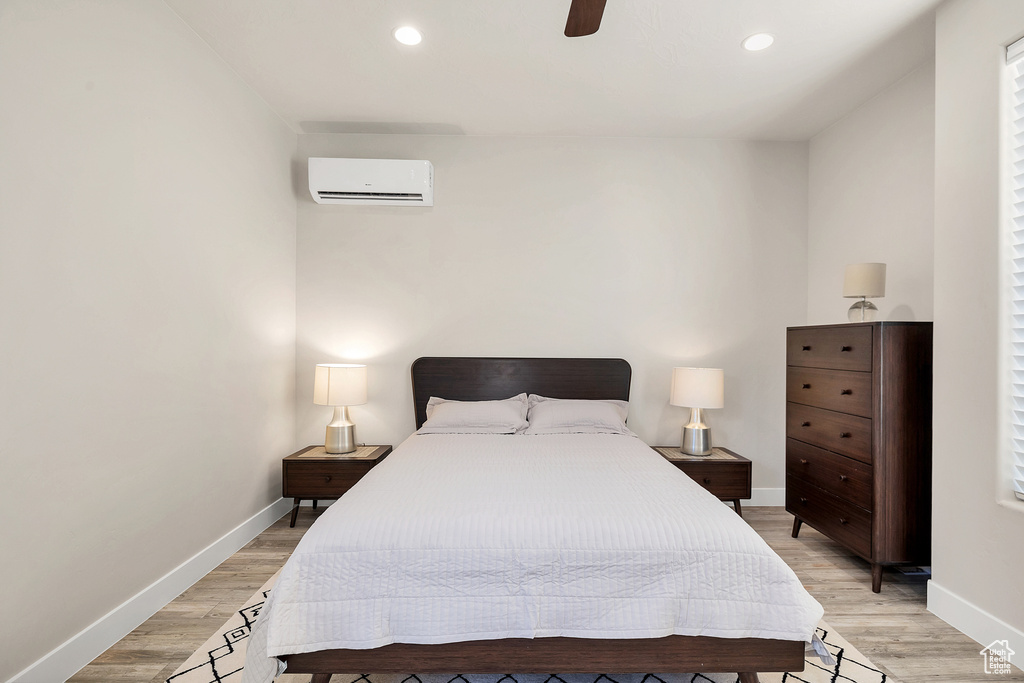 Bedroom with baseboards, light wood-type flooring, a wall mounted AC, and recessed lighting